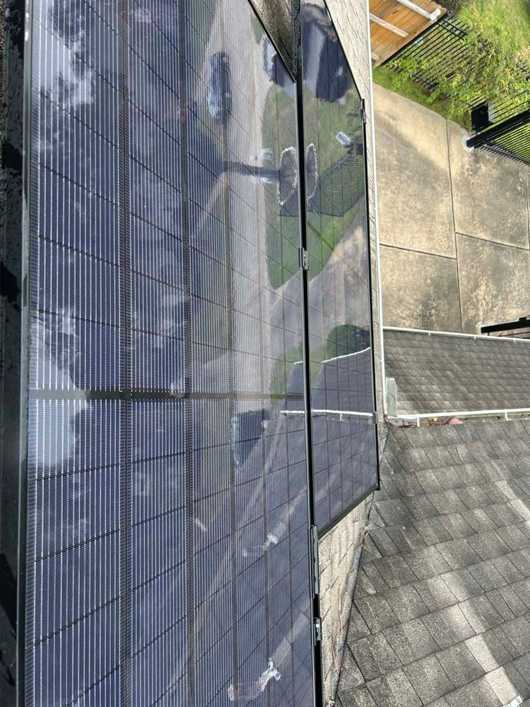 Solar panels mounted on a rooftop beside a concrete walkway and garden fence