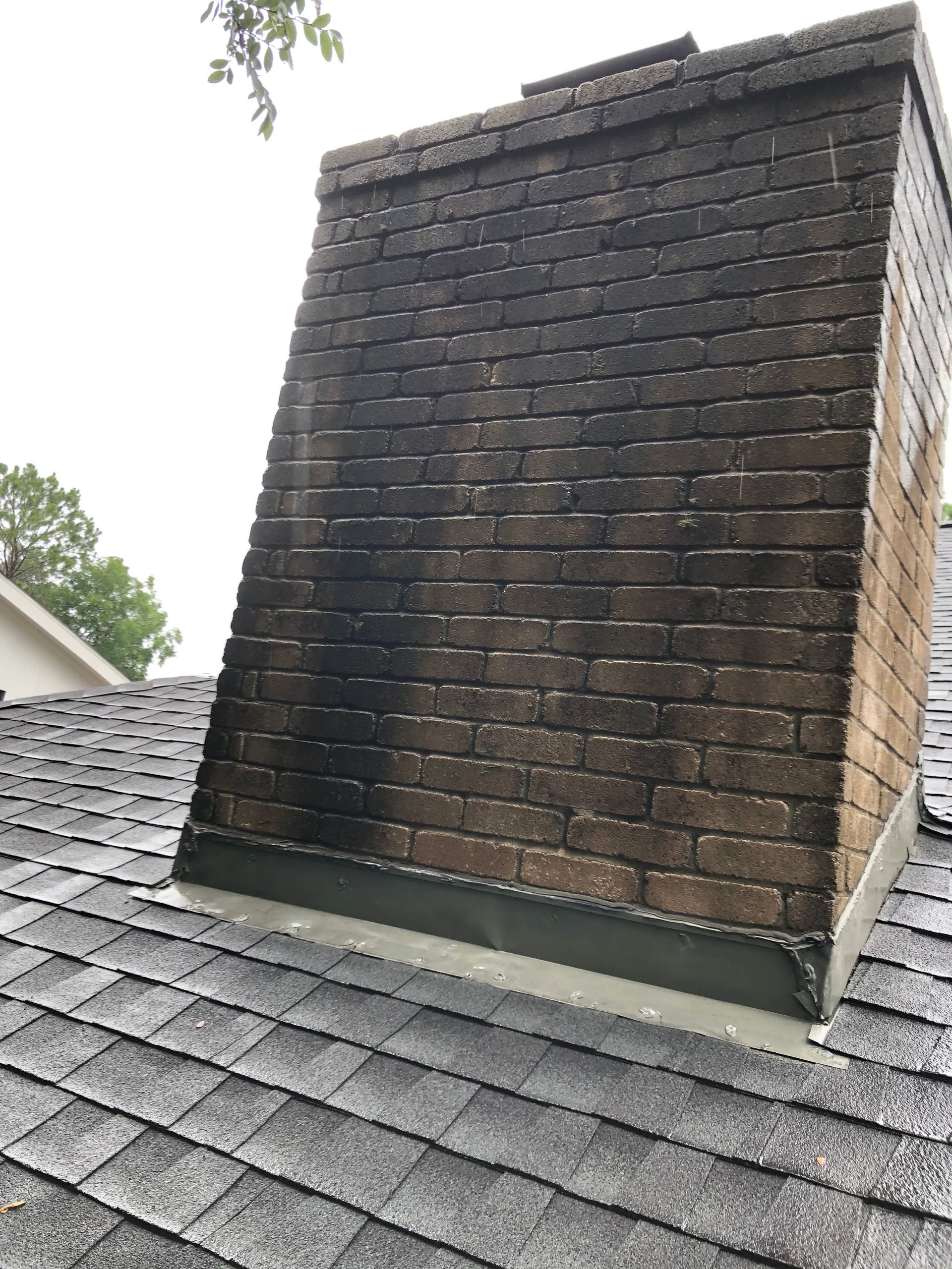 Weathered brick chimney rising from a gray shingled roof against an overcast sky