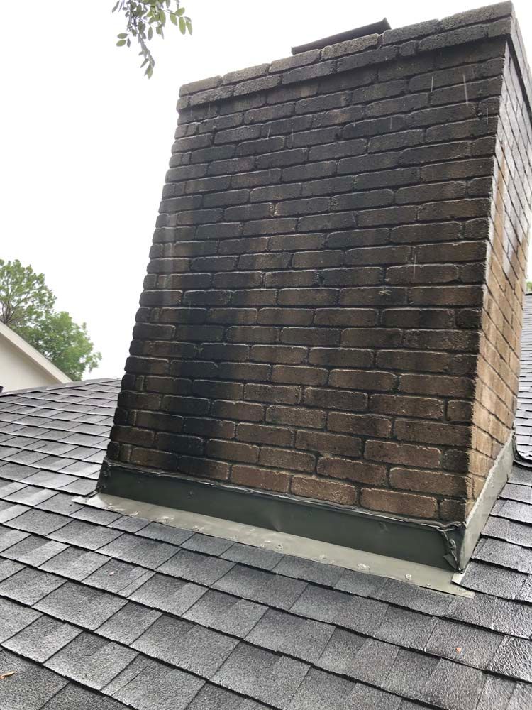 Brick chimney on a shingled roof, darkened with age and weather stains.