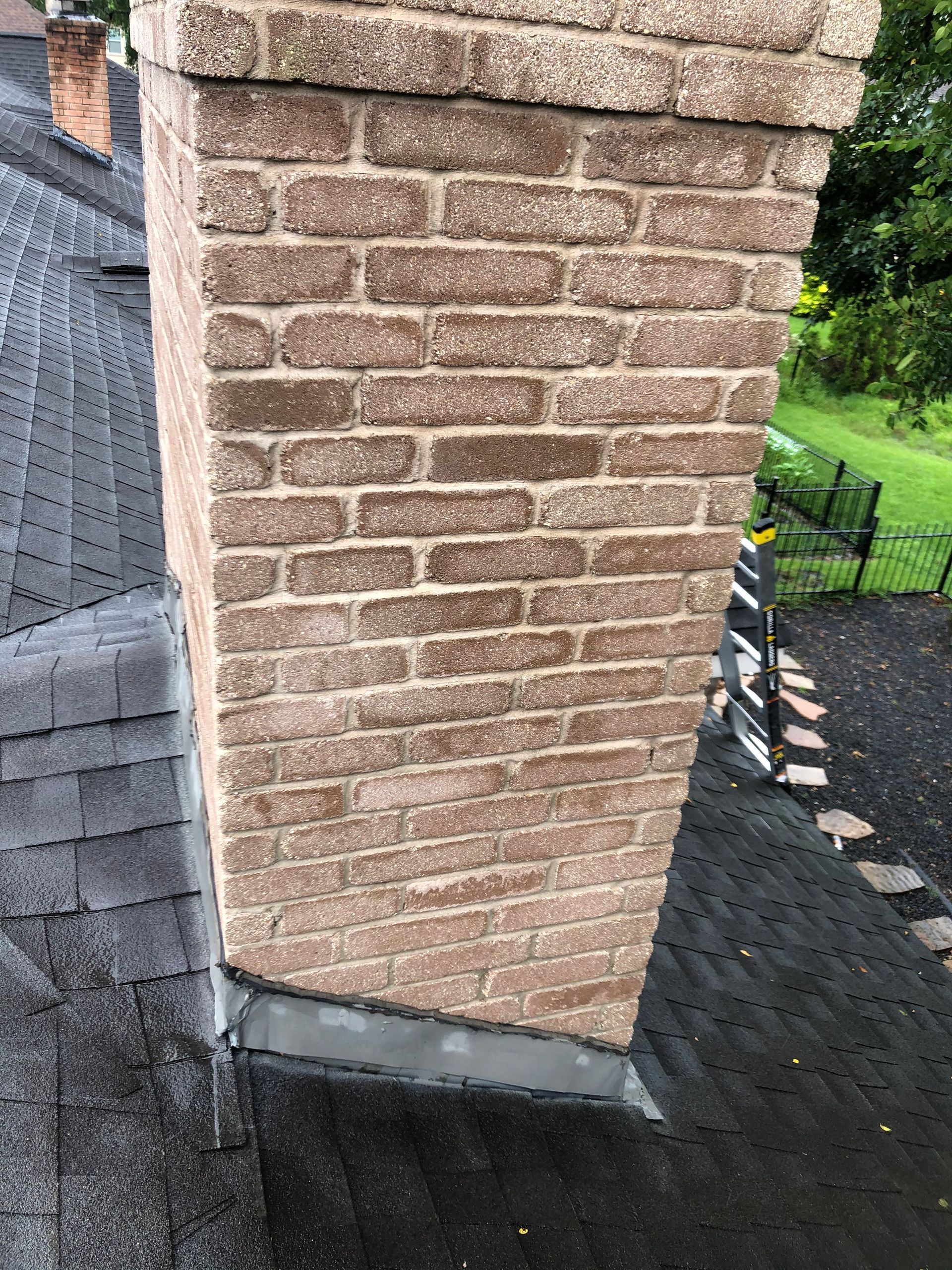 Brick chimney above a dark shingled roof, with a metal flashing base.