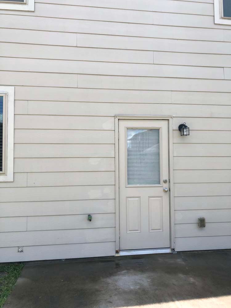 Exterior house wall with a white door, small window, and light fixture over a concrete patio.