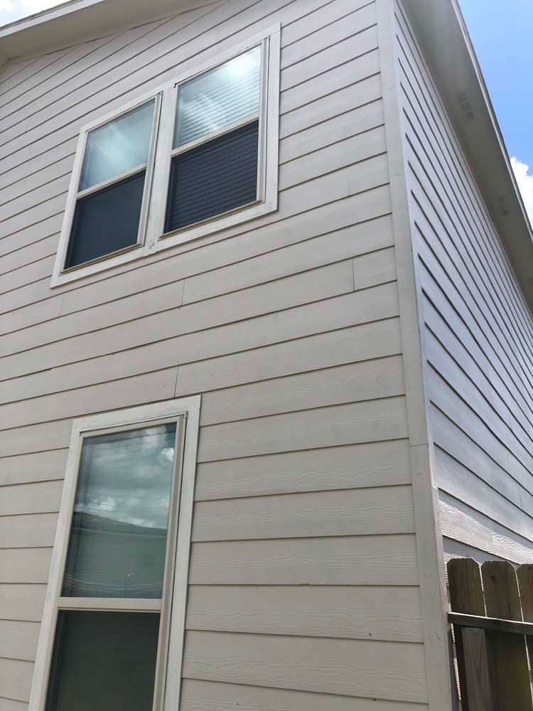 White vinyl-sided house exterior with two windows on the upper wall and one window below.