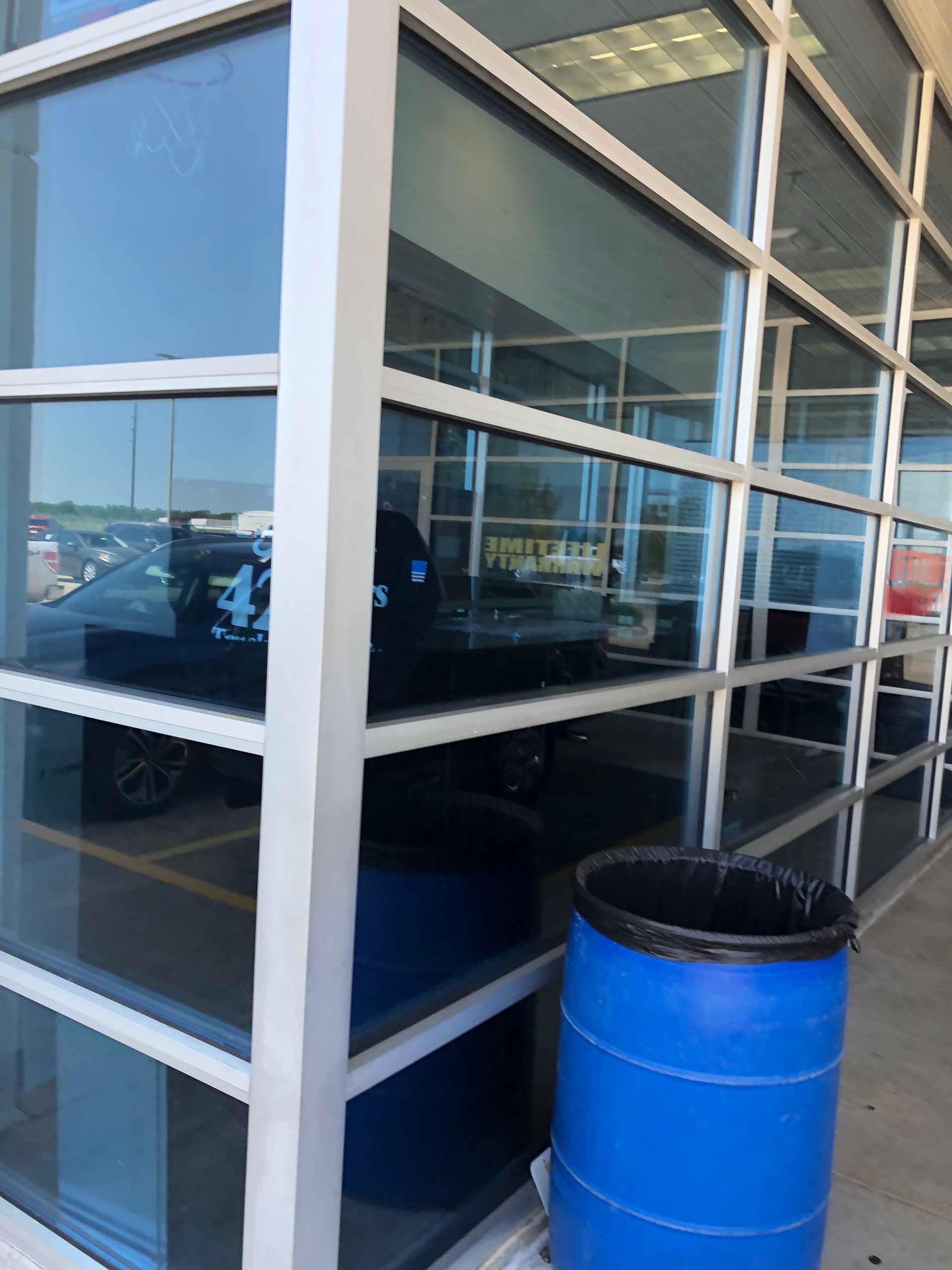 Glass storefront with a blue trash barrel outside and a vehicle reflected in the windows