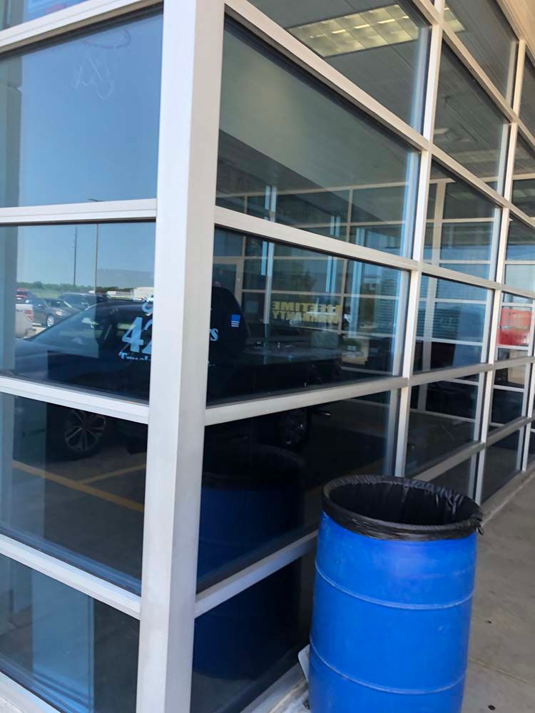 Glass storefront corner with white framing and a blue barrel trash can outside