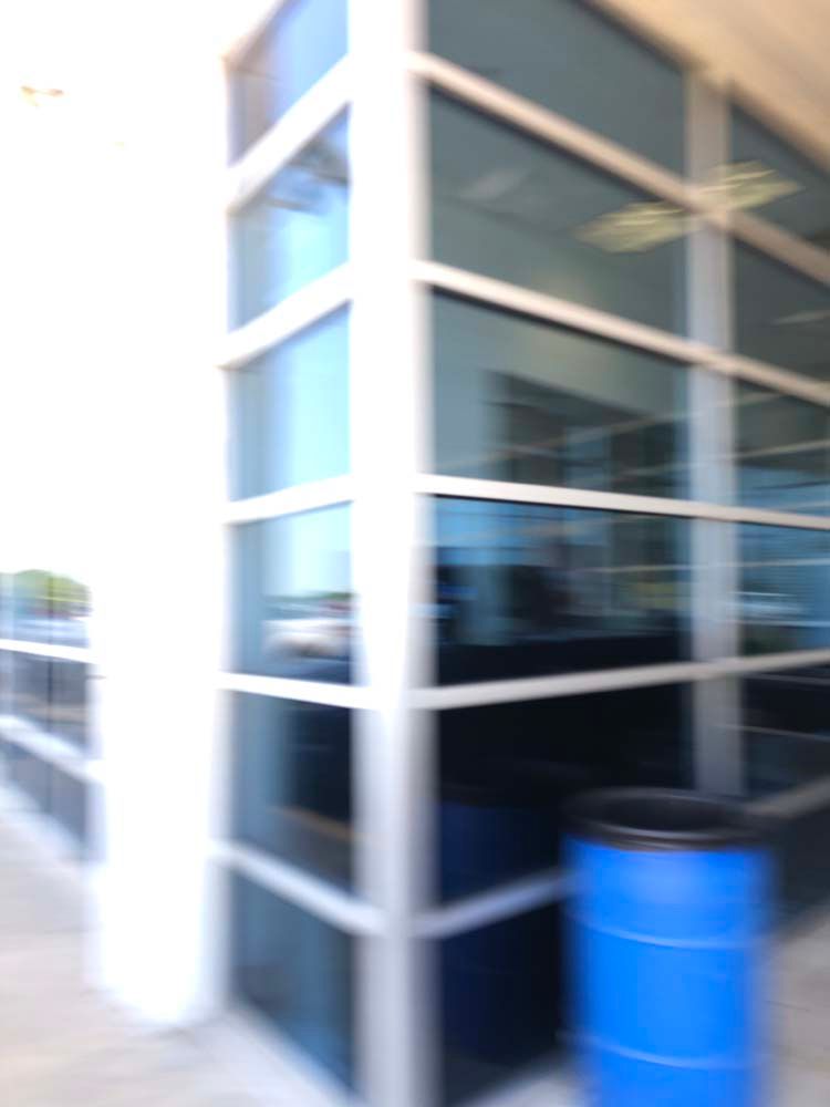 Glass storefront entrance with white framing and a blue barrel beside it