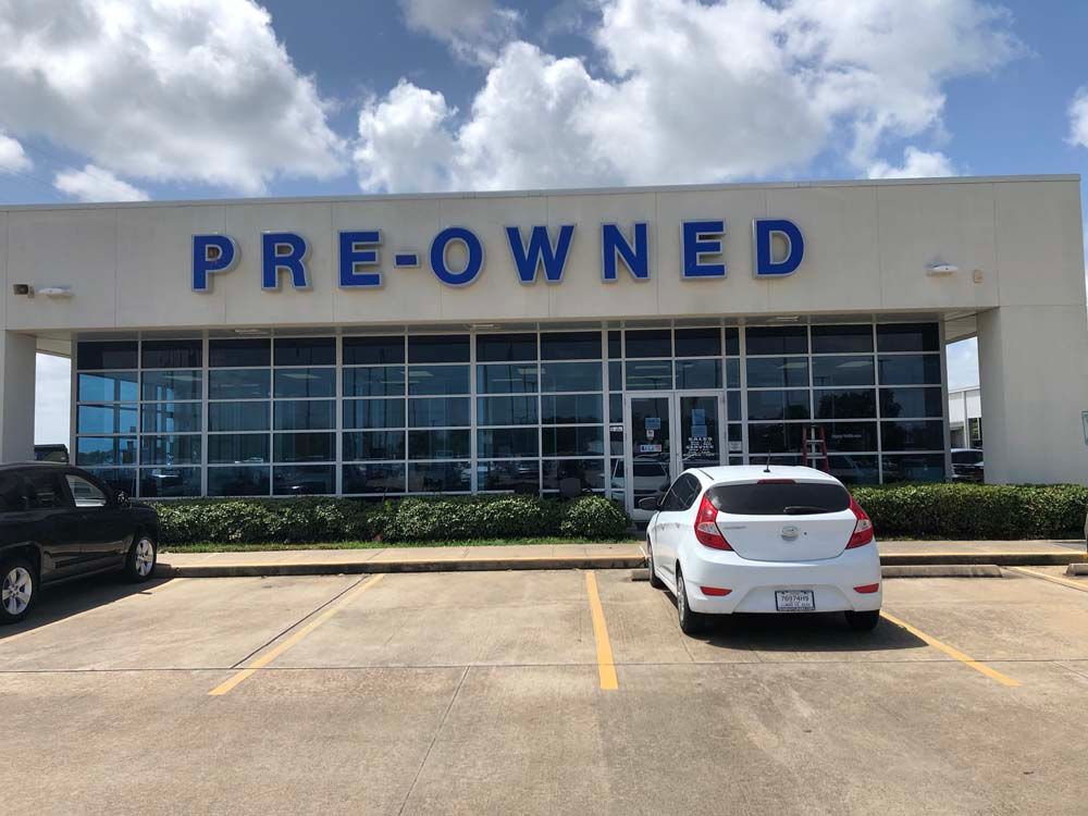 Pre-owned car dealership storefront with large blue sign and cars parked in front