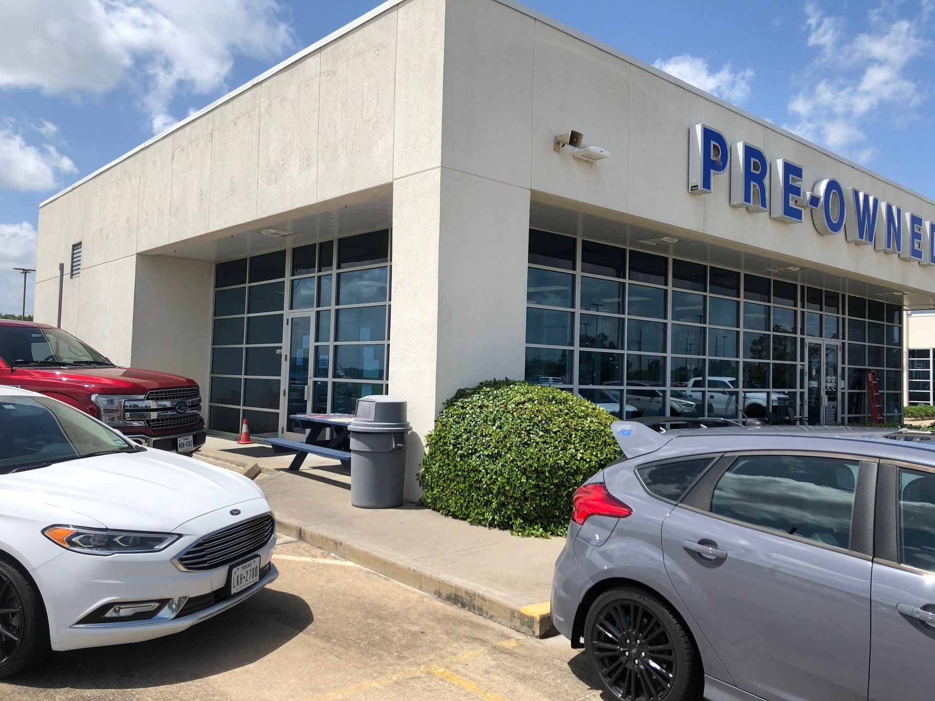 Car dealership exterior with parked cars and large glass showroom windows on a sunny day