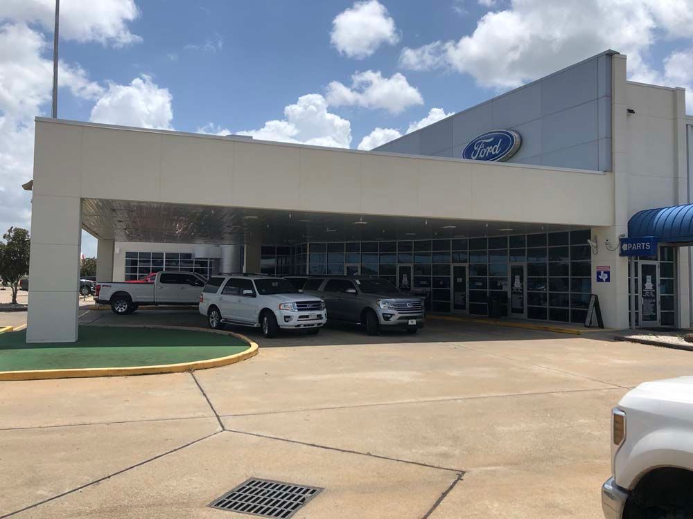 Ford dealership entrance with cars parked under a covered showroom on a sunny day