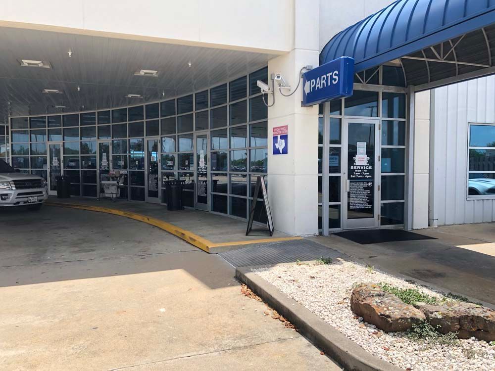 Car dealership service entrance with blue awning, glass doors, and a curbside planter