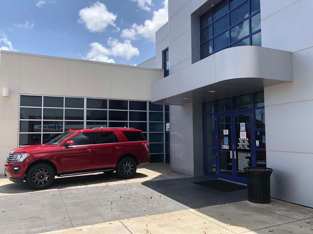 Red SUV parked beside a modern building entrance under a blue sky with clouds