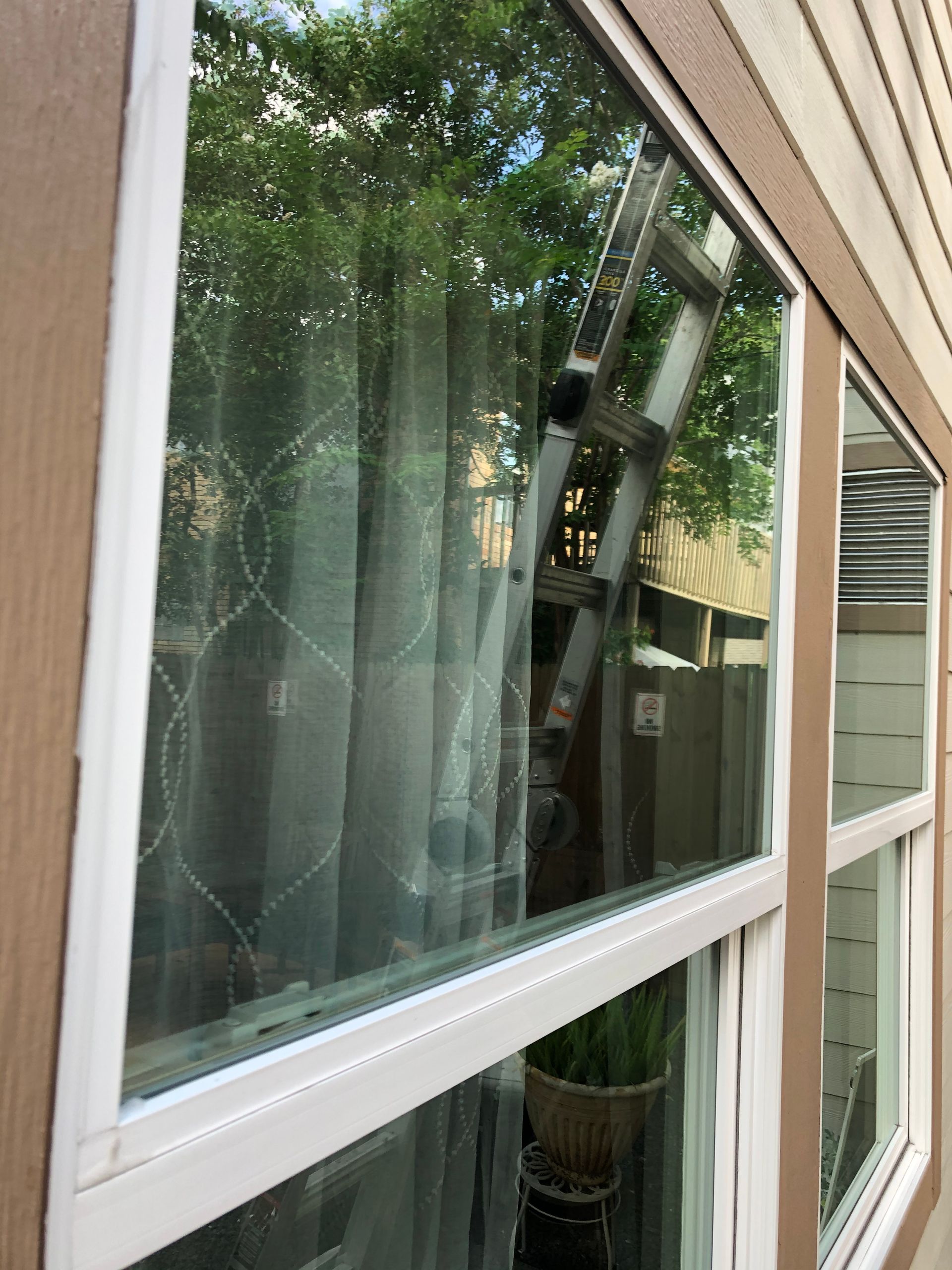 Broken window screen on a house exterior, with a ladder reflected in the glass.