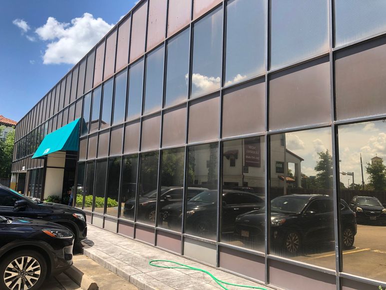 Glass-front commercial building with teal awning and parked cars under a blue sky