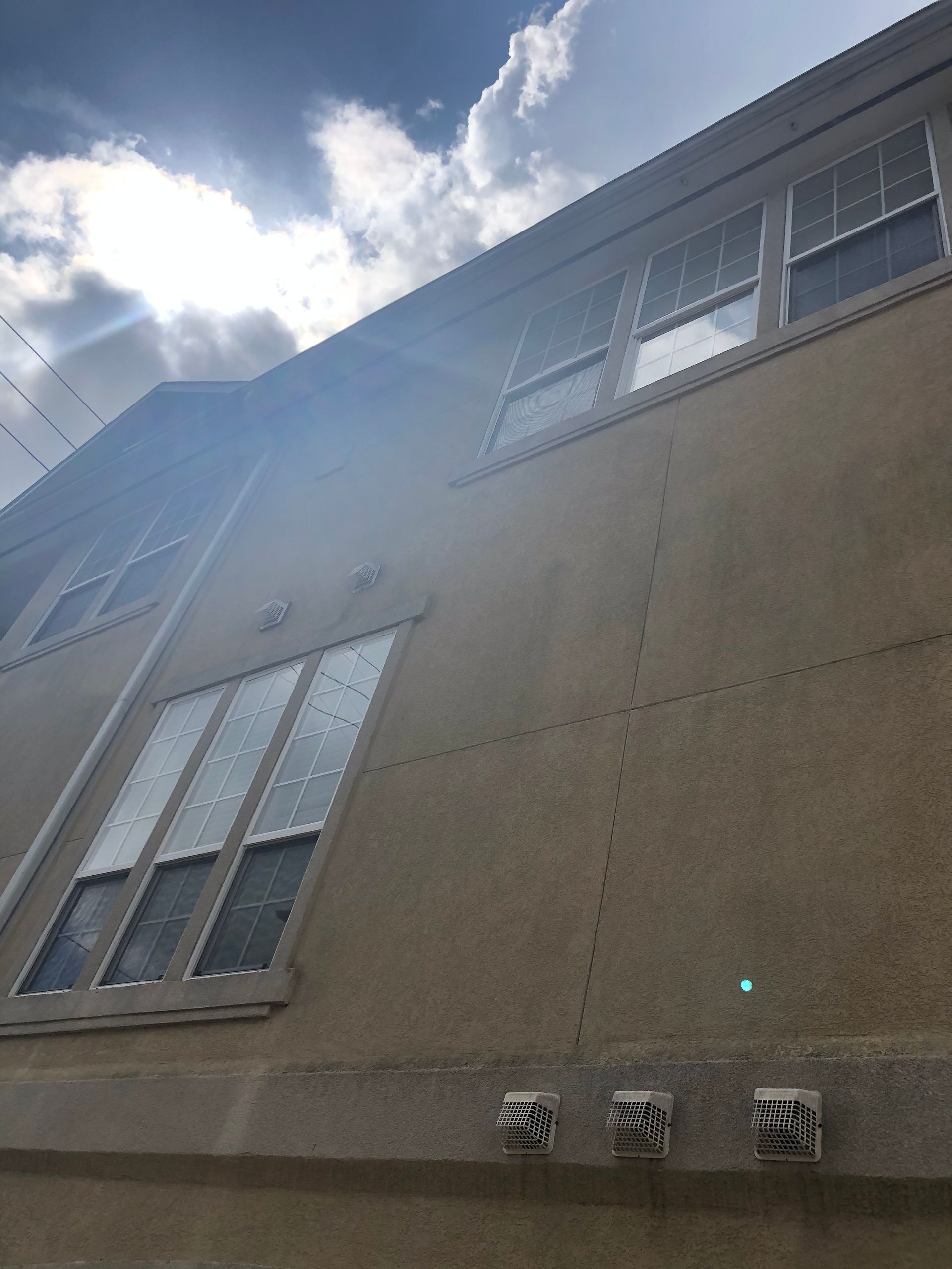 Low-angle view of a concrete building facade with windows against a bright cloudy sky.