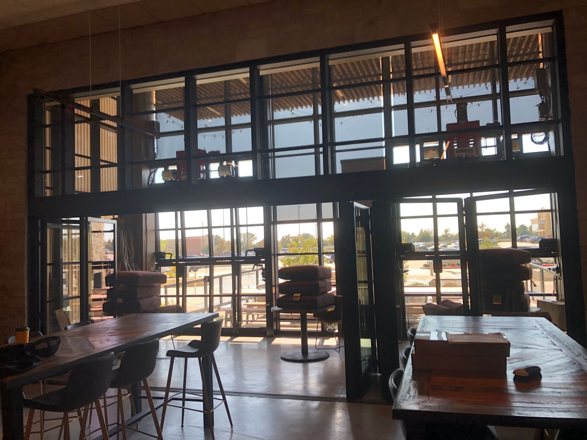 Sunlit café interior with tables, chairs, and large glass windows overlooking the outdoors