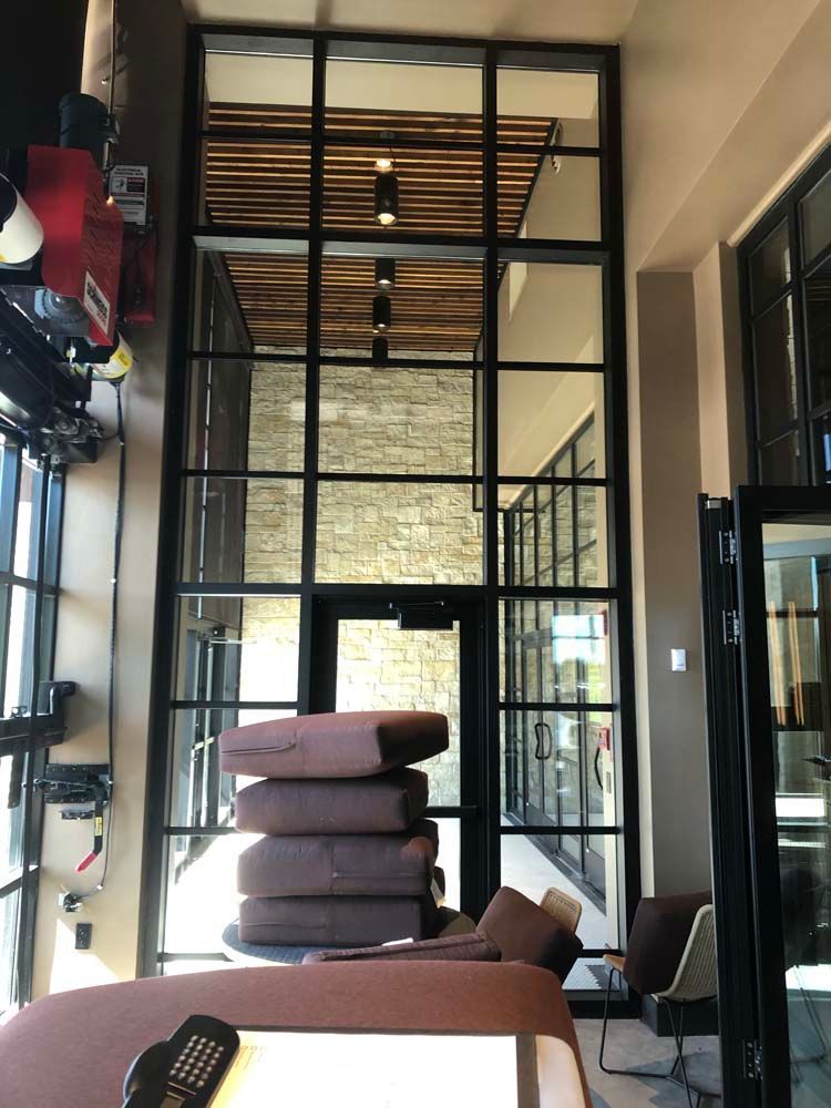 Modern lounge with tall glass partition, stacked brown cushions, and chairs in warm indoor lighting