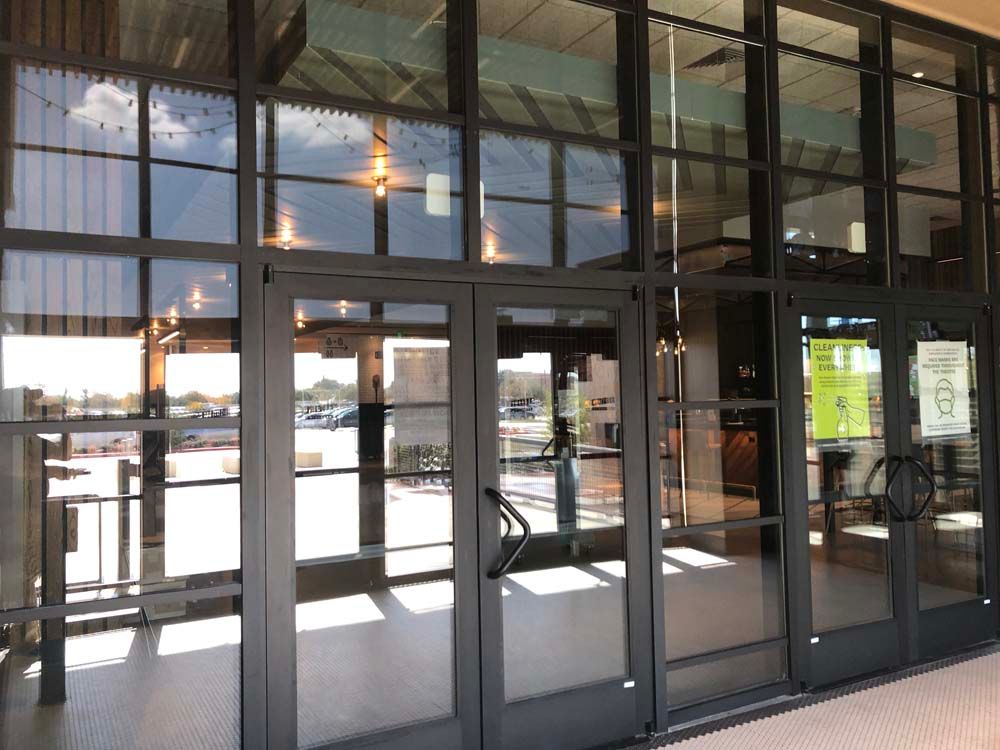Glass storefront entrance with sliding doors and reflections under a covered walkway