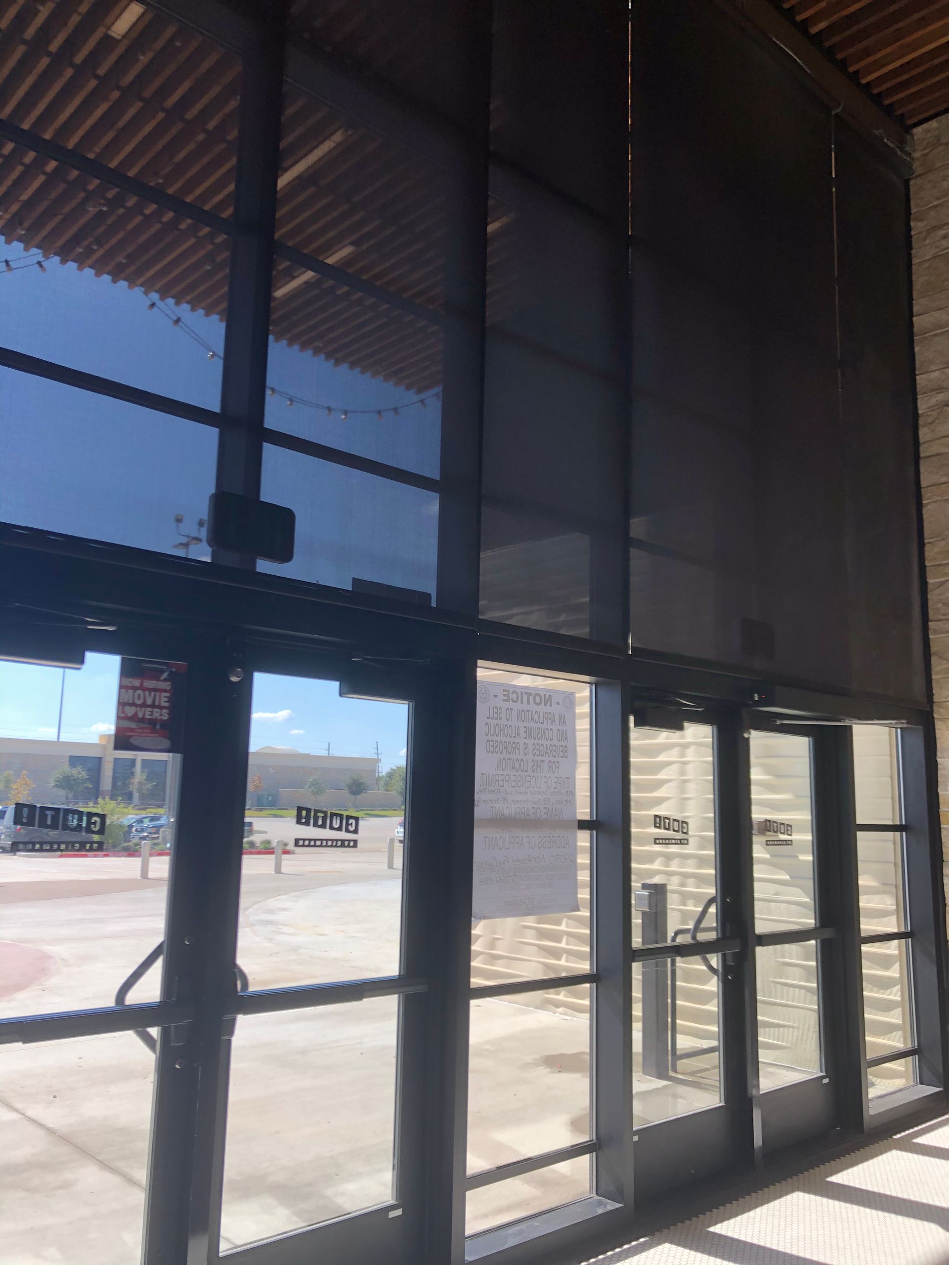 Sunlit glass storefront with dark metal blinds and a concrete walkway outside