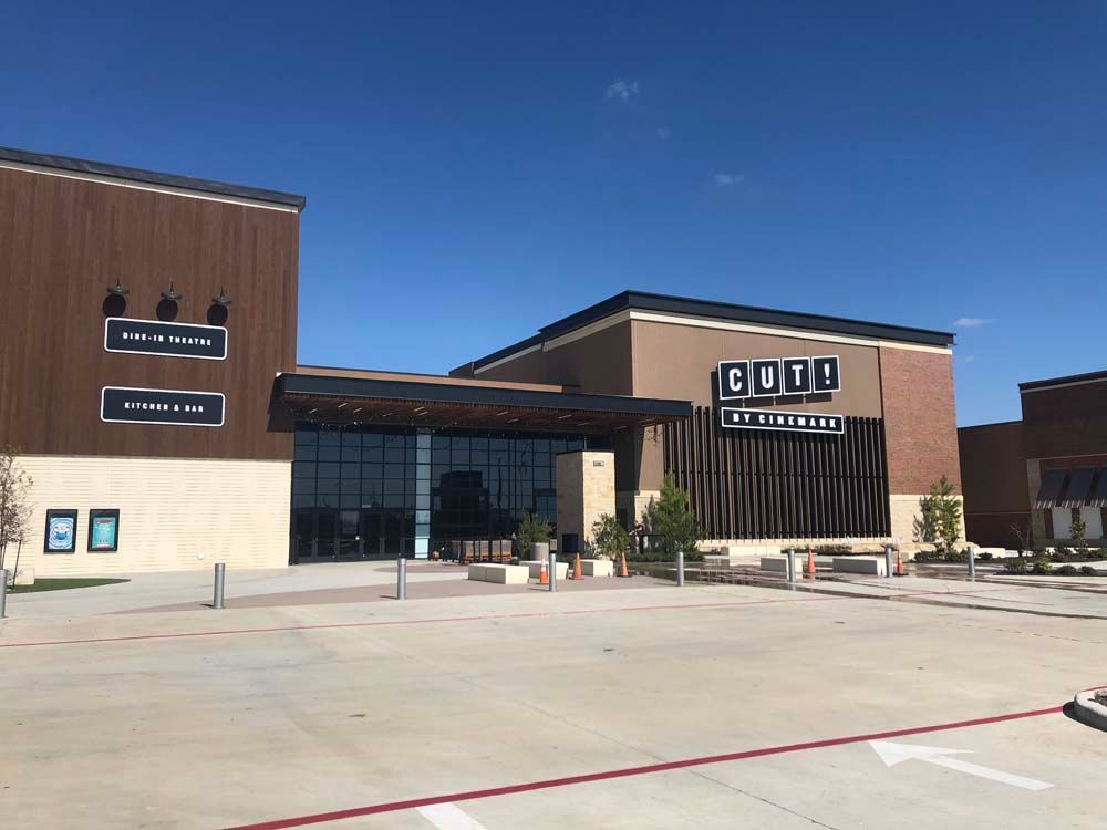 Modern brick storefront with glass entrance and large parking lot under a clear blue sky