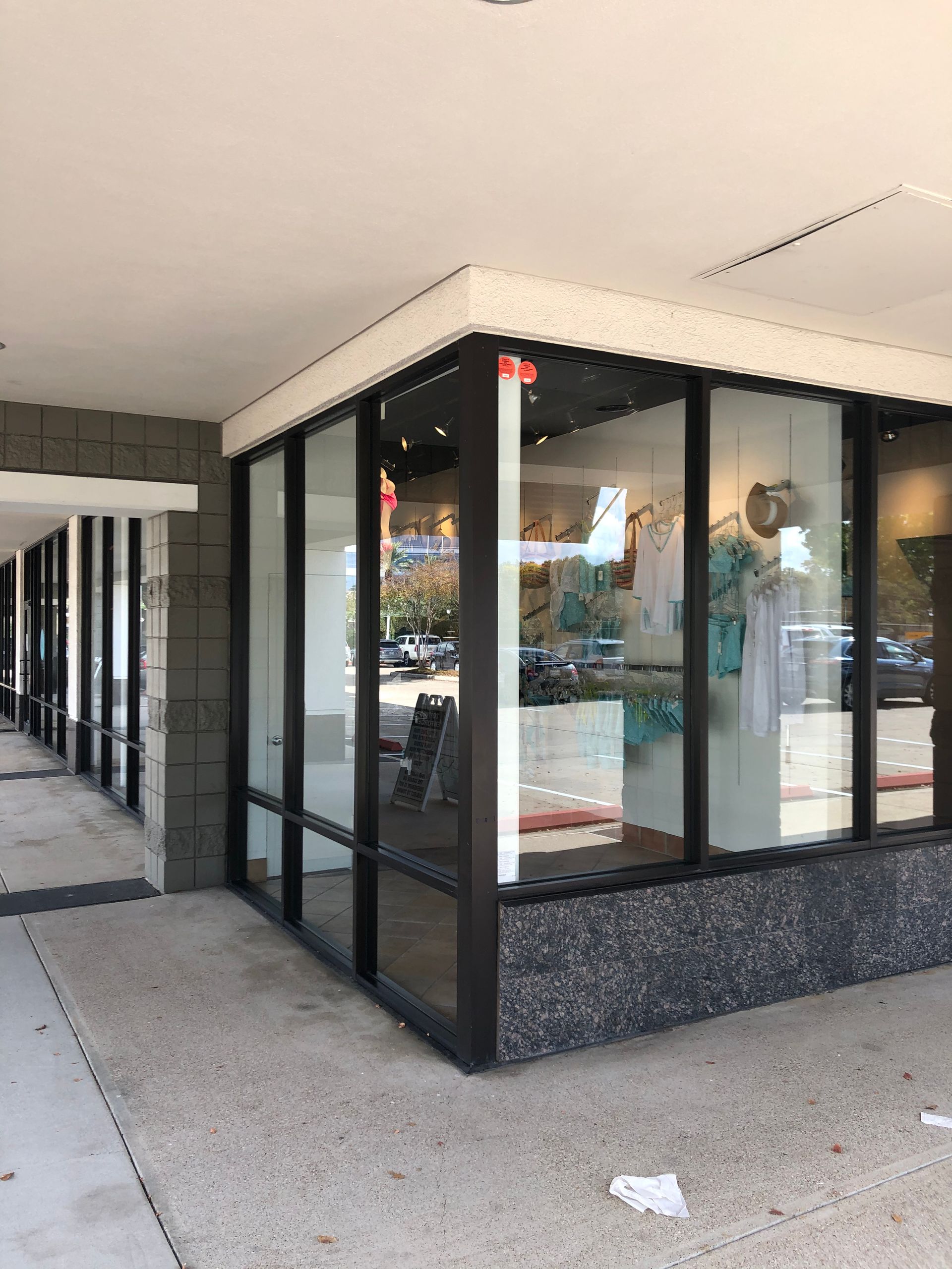 Corner of a storefront with large black-framed glass windows and a covered sidewalk.