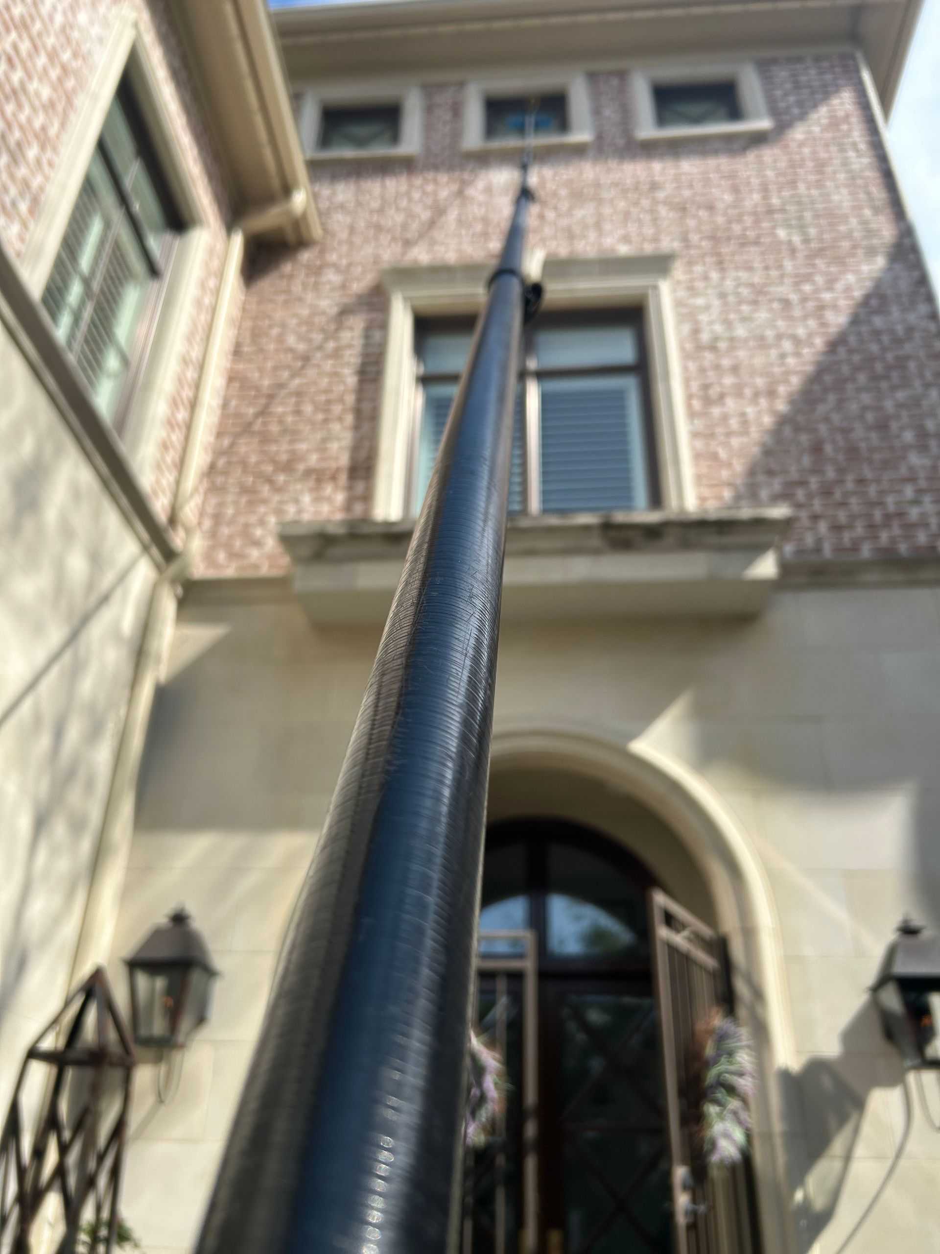 Upward view of a tall black utility pole beside a brick building with arched doorway and windows