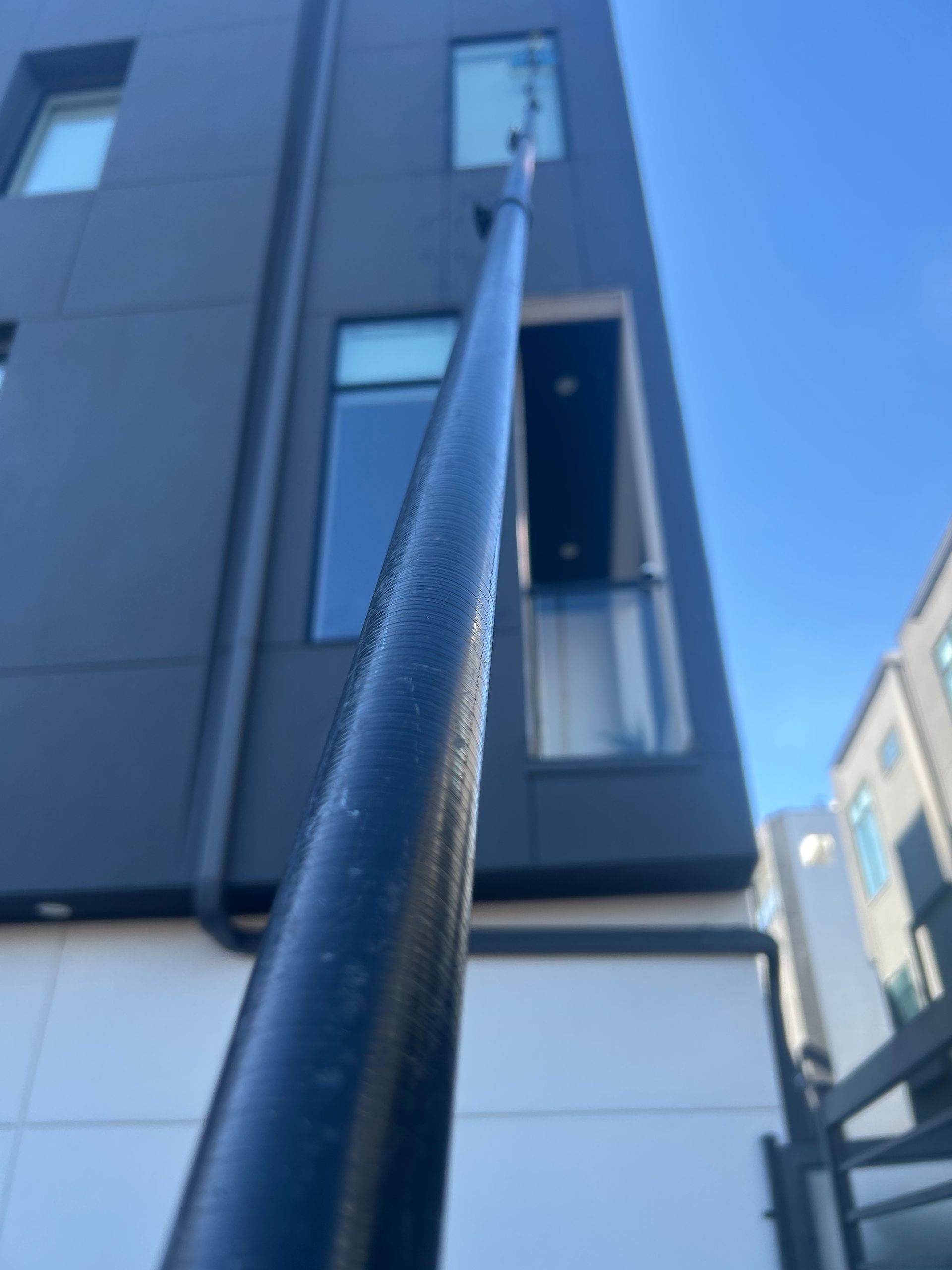 Long pole reaching up to a third-floor apartment window on a modern building