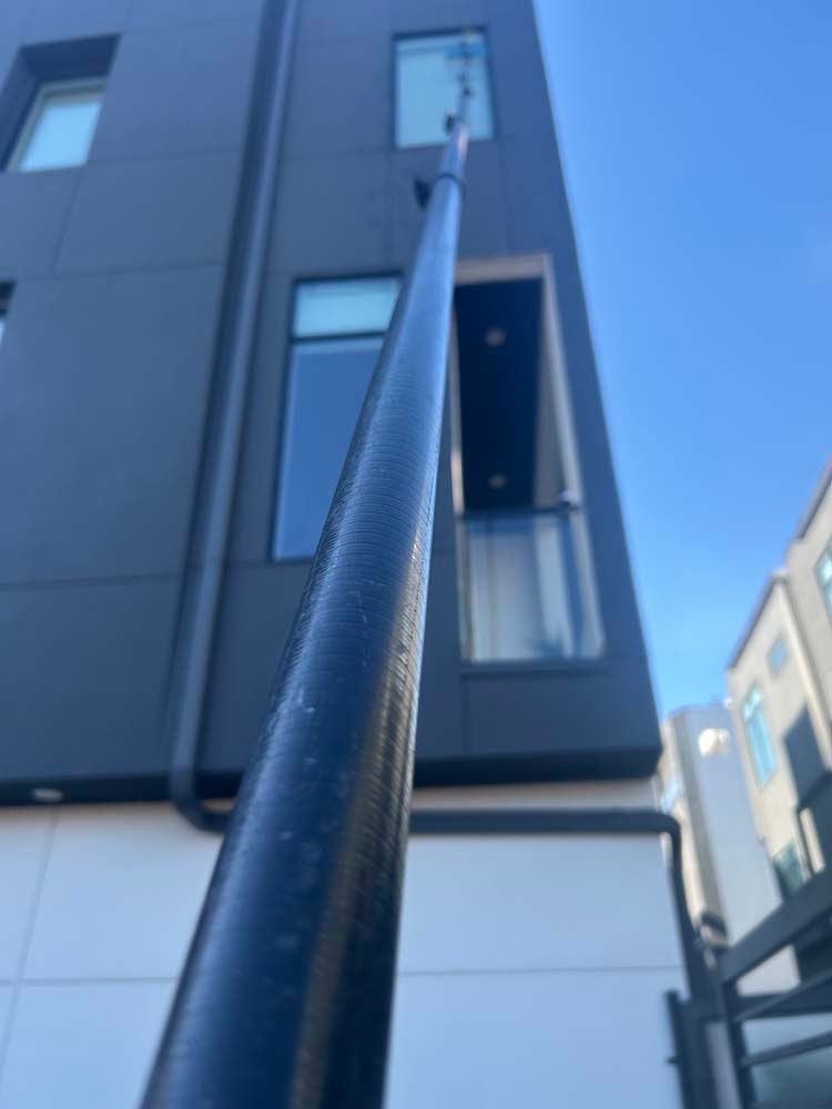 Tall pole reaching to an upper-floor window on a modern gray building under a blue sky