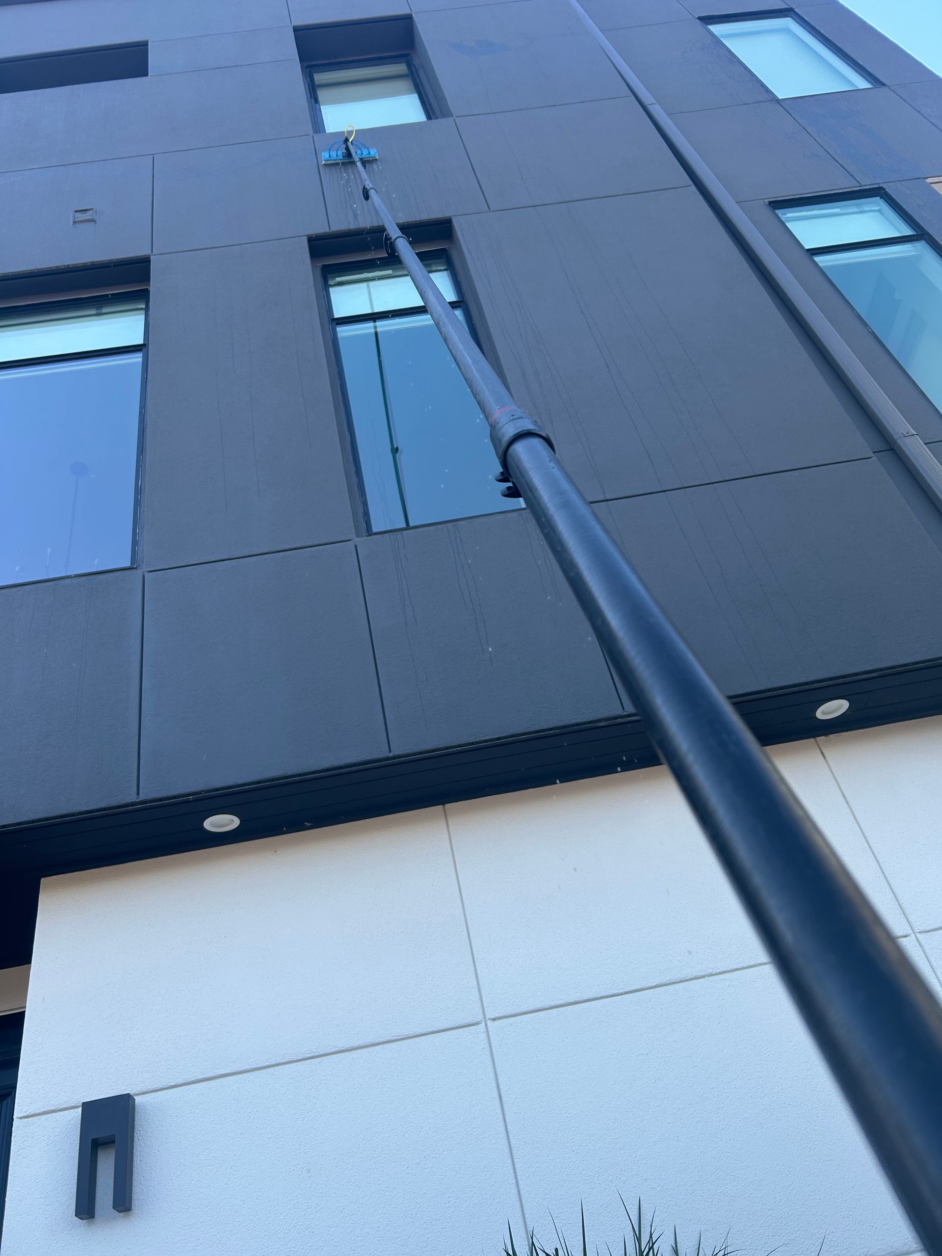Low-angle view of a modern building facade with a tall black pole reaching toward upper windows.