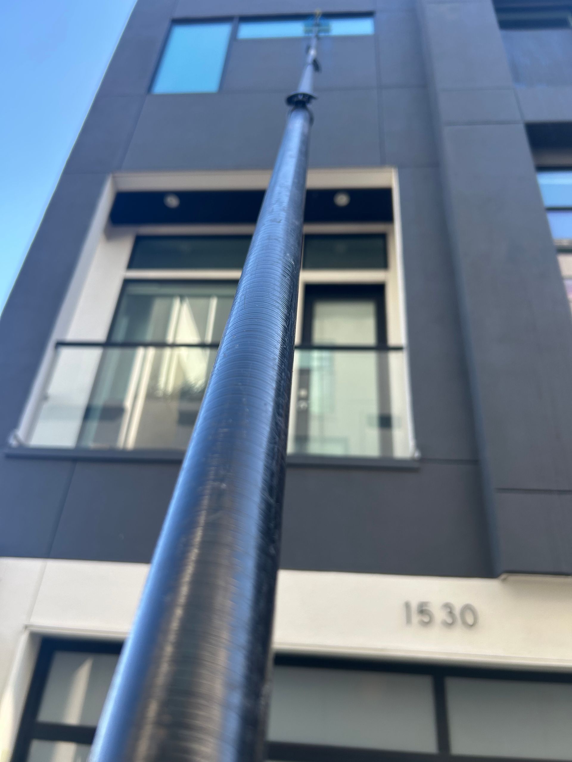 Low-angle view of a building facade with a tall pole in front and the number 1530 visible above a window.