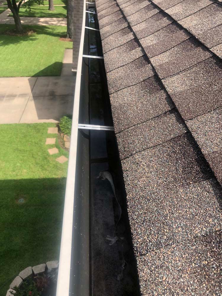 Close-up of a roof gutter beside shingles, overlooking a green lawn and walkway below