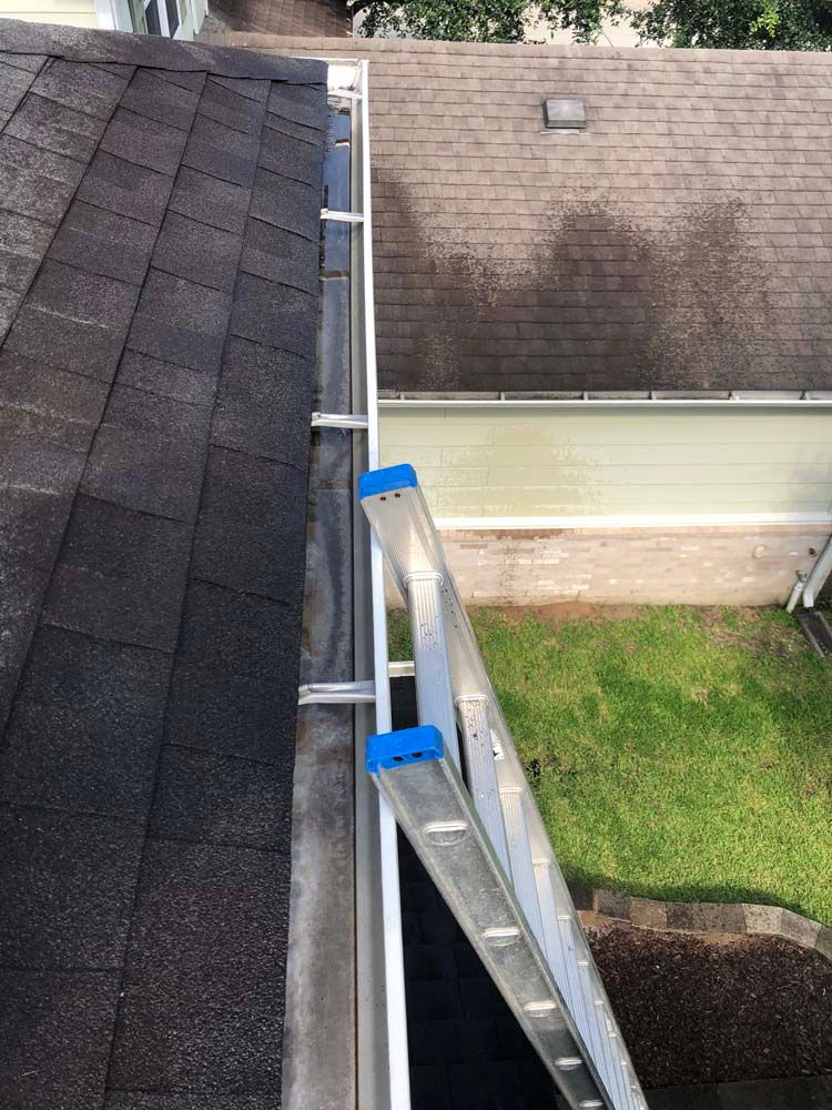 Extension ladder leaning from a roof to a lower roof beside a house and lawn