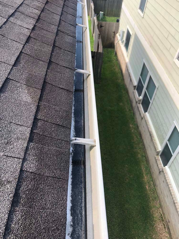 Rooftop gutter and roof shingles beside a beige building in a narrow grassy alley