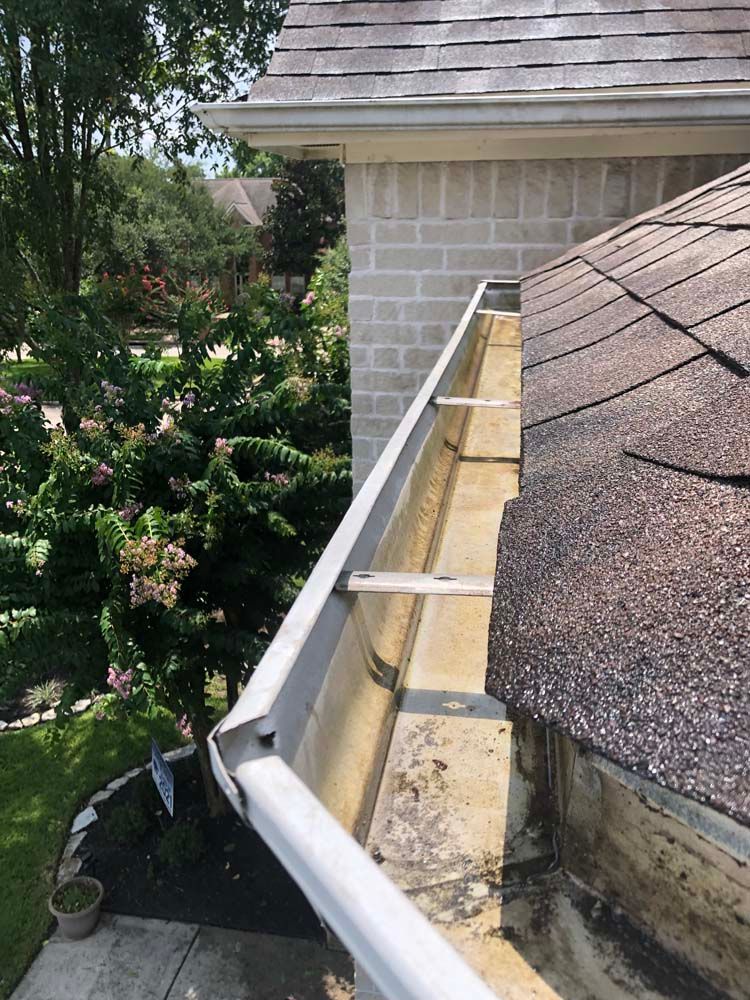 Roof gutter beside shingled roof and brick wall, with white downspout on a residential house.