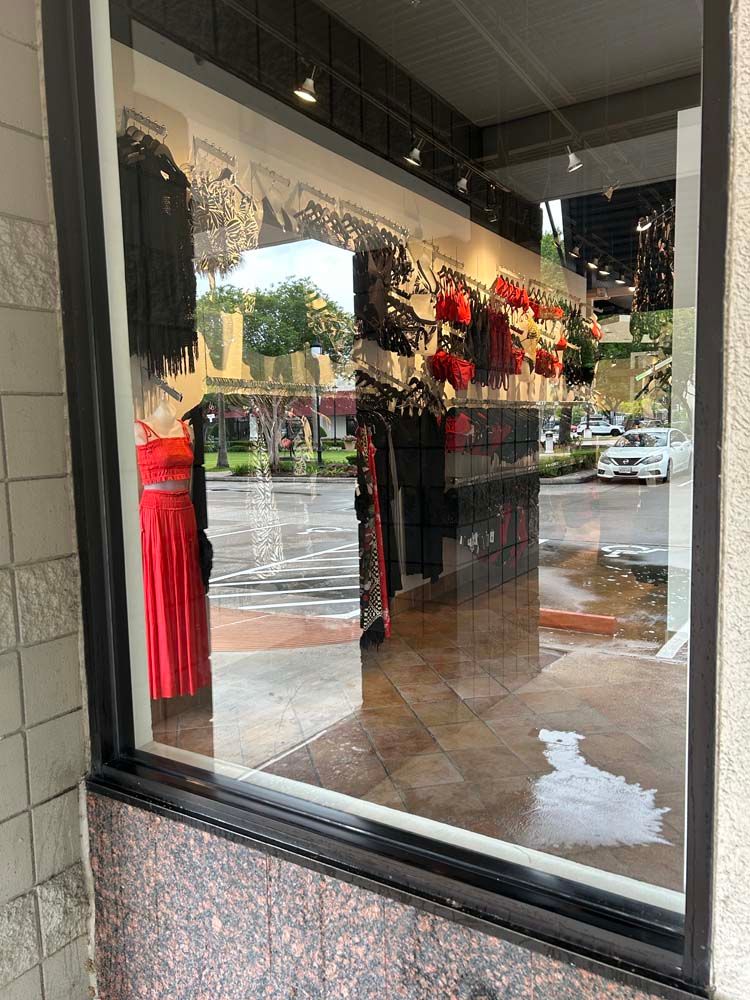 Clothing store window display with red dresses and black outfits reflected on a wet street
