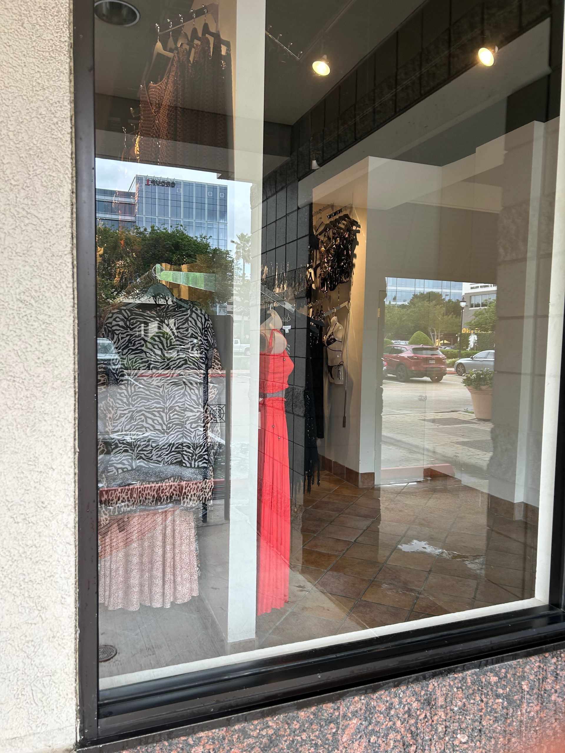 Storefront window reflecting a street view, with a bright pink dress inside the display.
