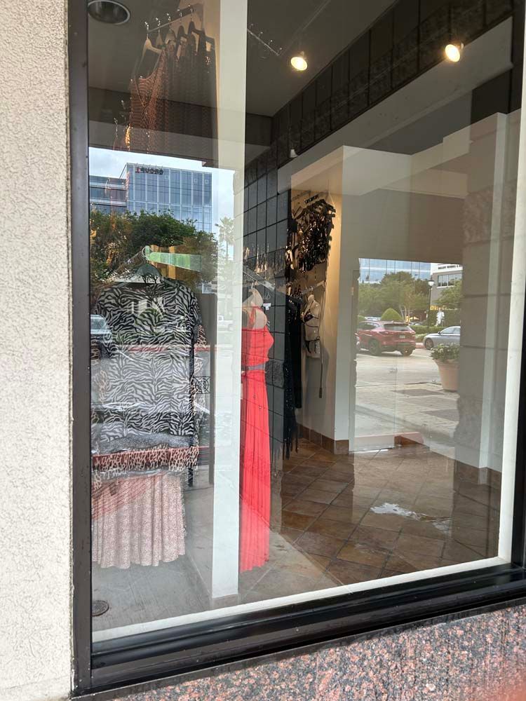 Storefront window display with a bright pink dress and reflections of the street outside