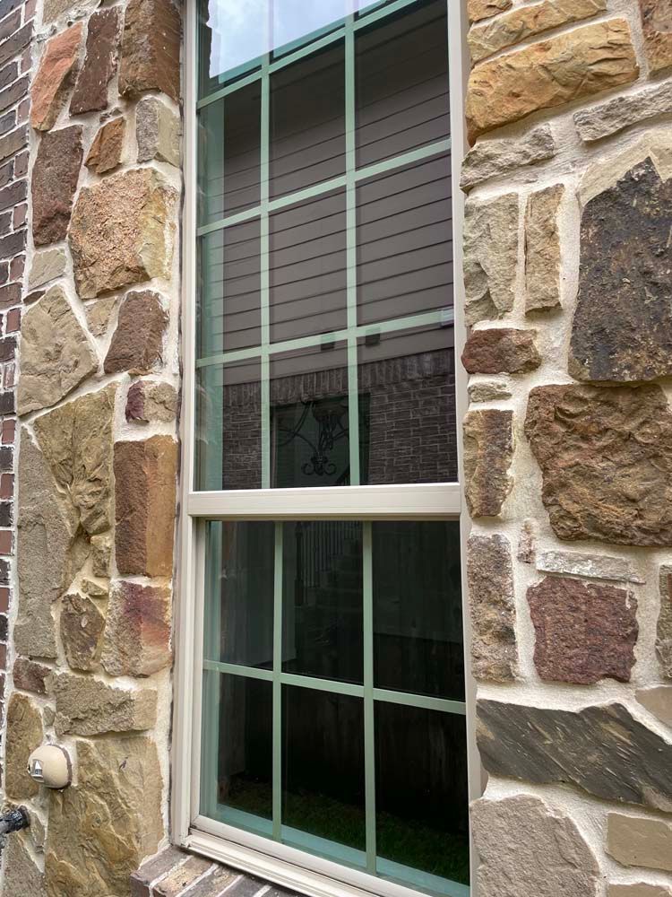 White-framed window set in a stone wall with green muntins and closed blinds inside