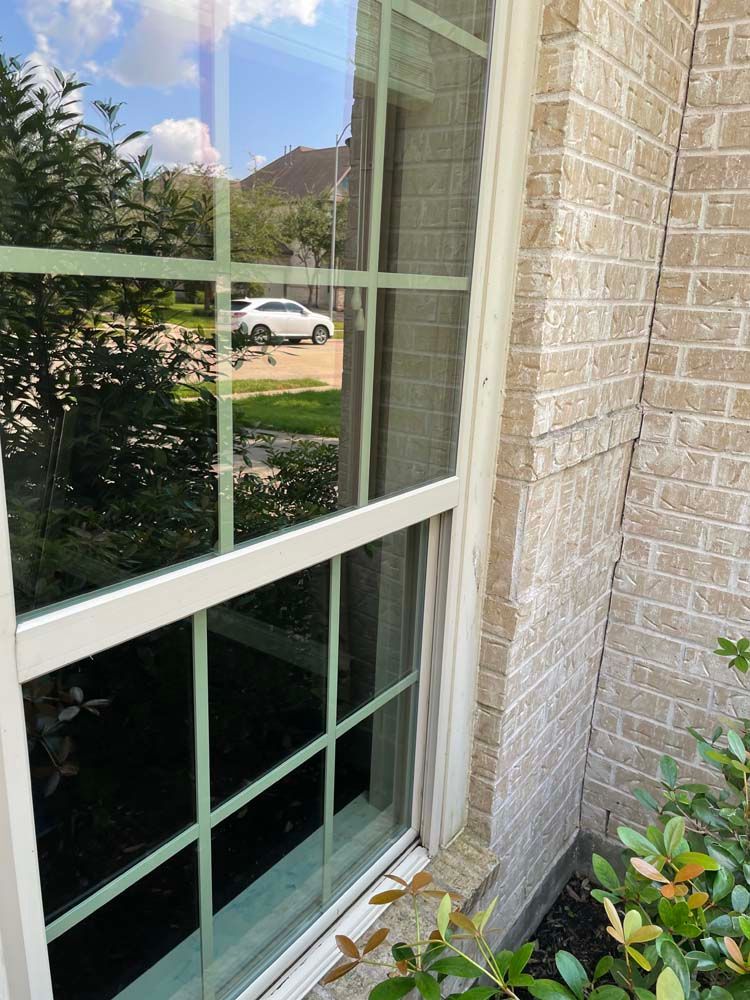 Close-up of a white-framed window beside a brick wall, reflecting a white car and greenery outside