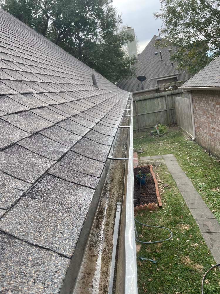 Roofline with gray shingles and gutters above a narrow backyard and grass path.