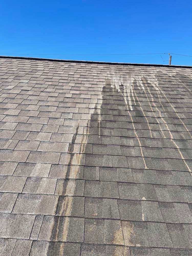 Roof shingles with dark water stains running downward under a clear blue sky
