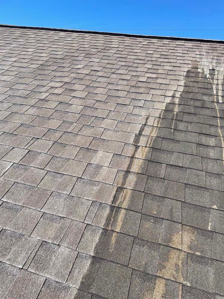 Shingled roof with a dark water stain on the right side under a blue sky