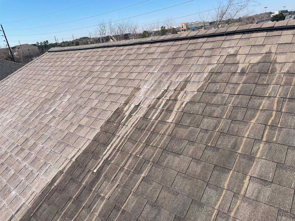 Shingled rooftop with visible water stains and weathered patches under a clear sky