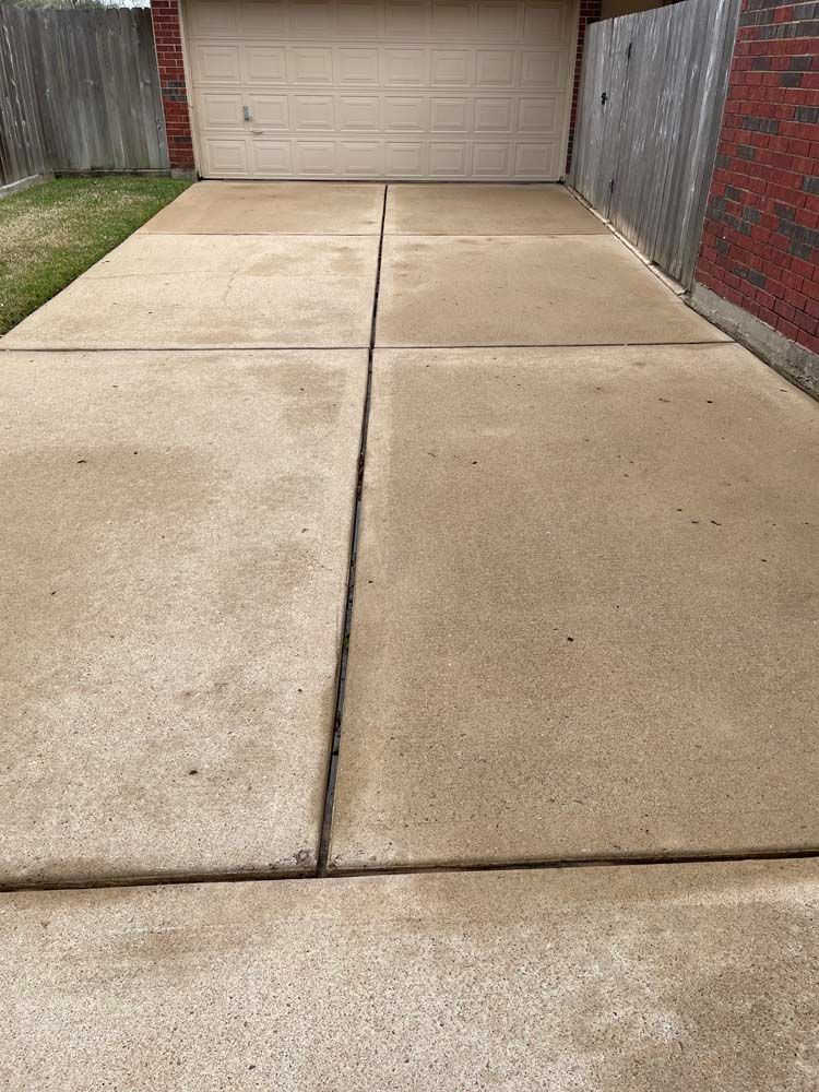 Concrete driveway leading to a closed garage door, bordered by a fence and brick wall.