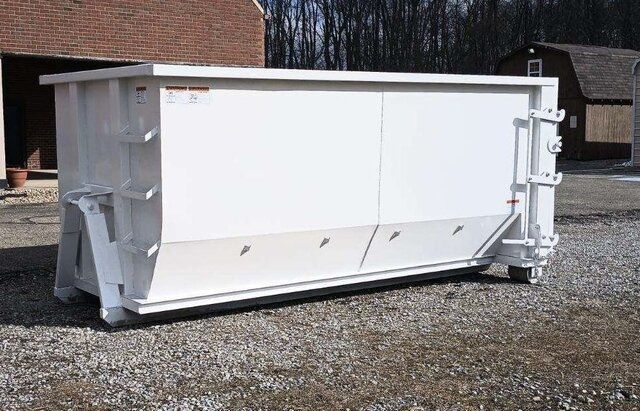 White industrial dumpster on gravel beside a brick building.