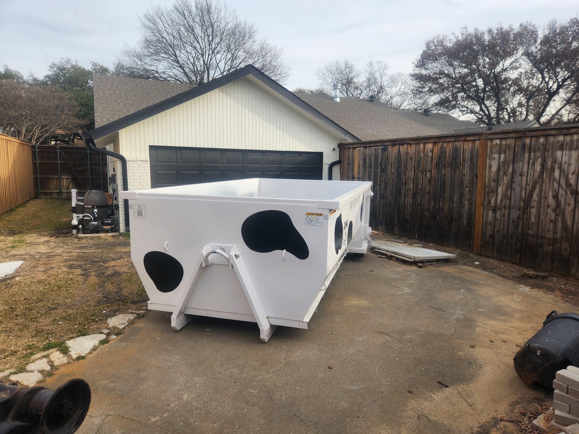 White trailer in a driveway with black patches, in front of a garage and wooden fence