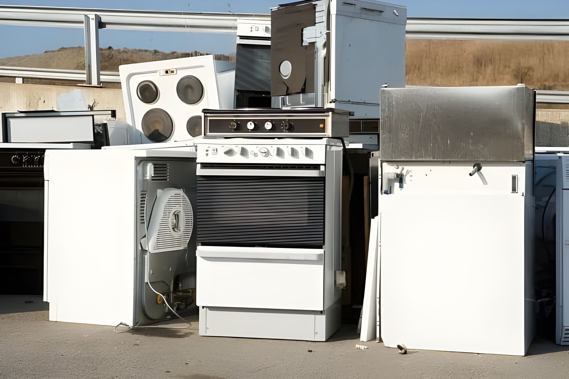 Pile of old appliances and kitchen equipment outdoors in a junkyard or salvage yard.