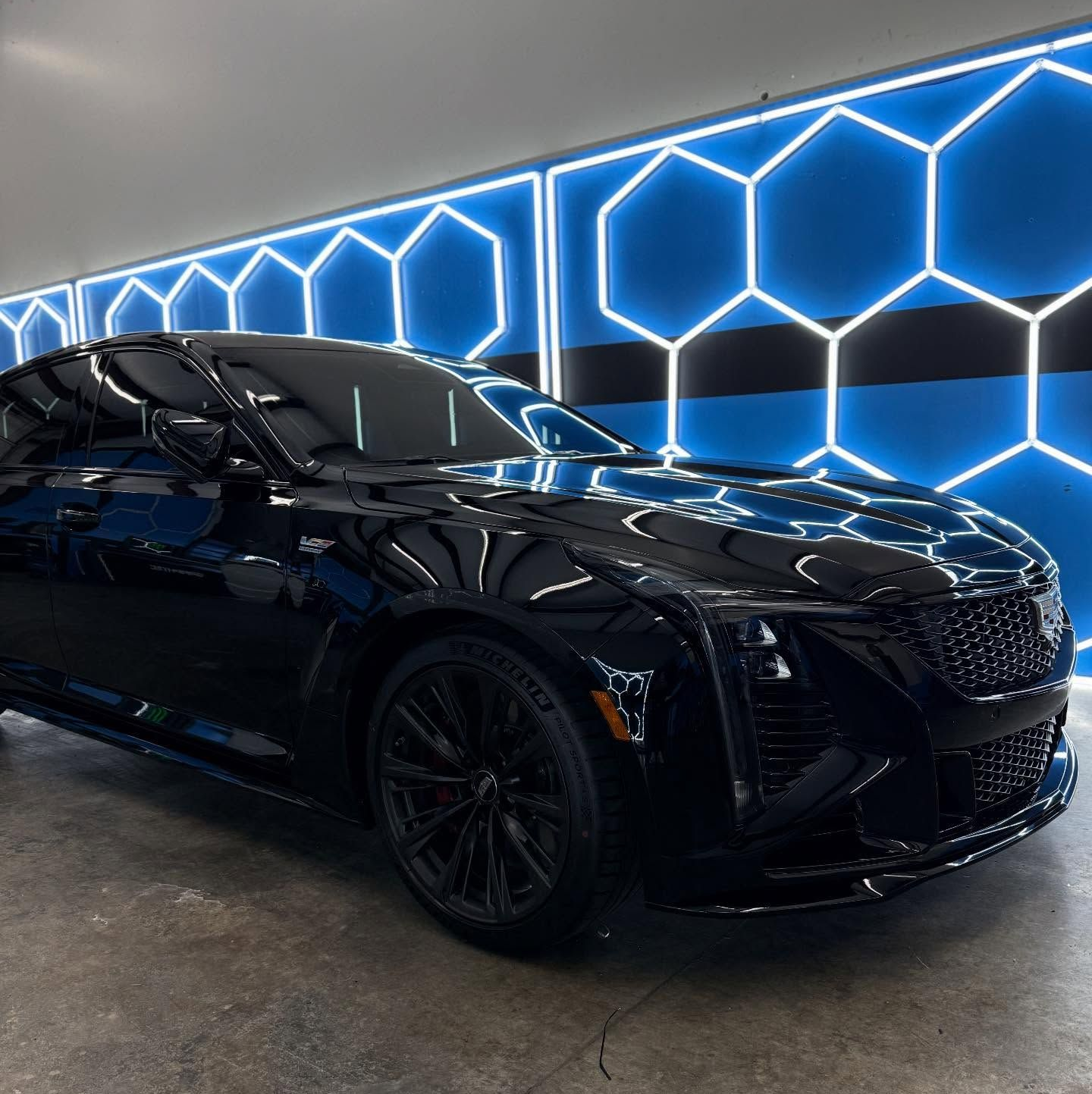 Black Cadillac sedan in a garage with blue hexagon lighting on the wall.