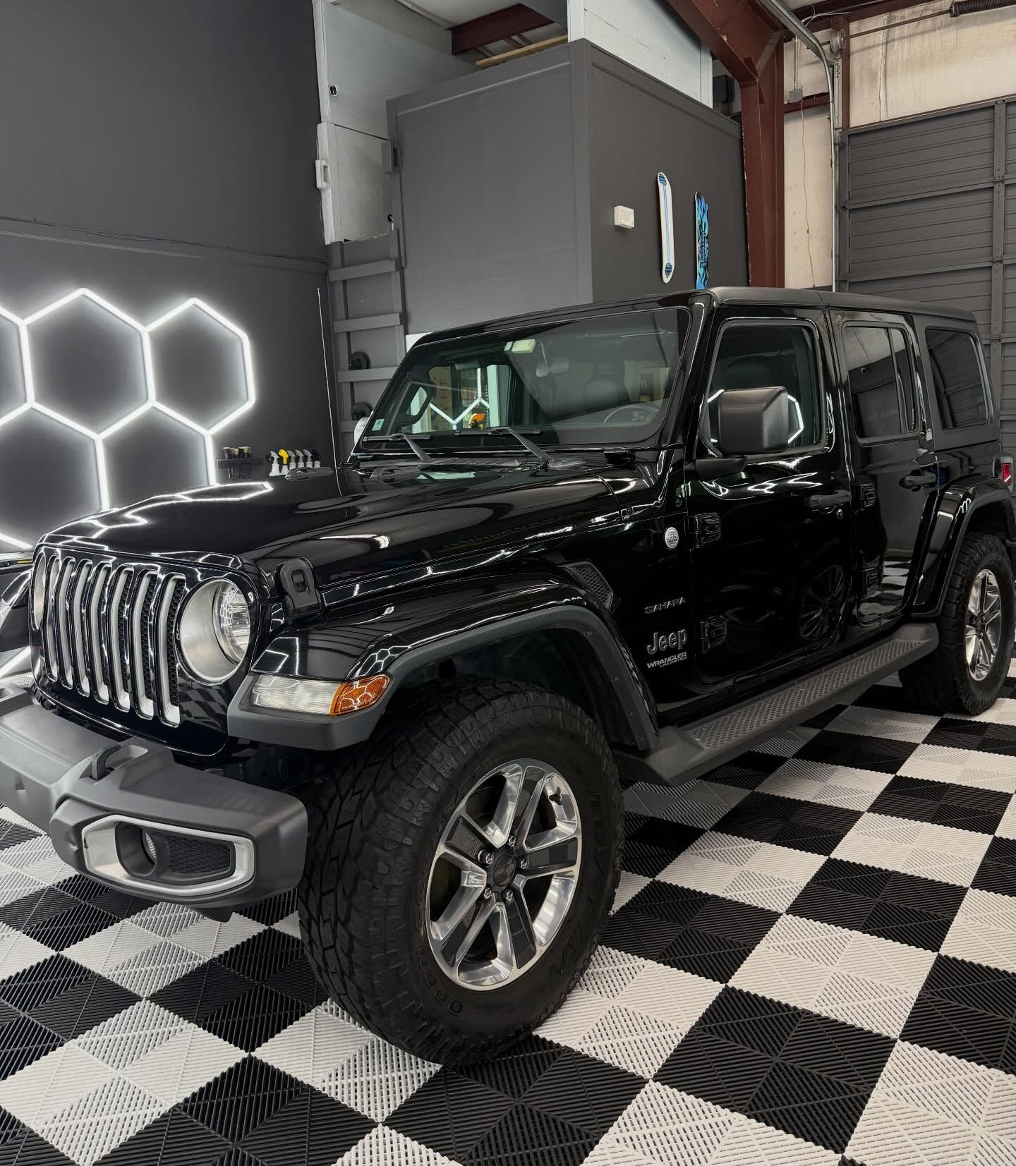 Black Jeep Wrangler parked in a garage with checkered floor and hexagonal lights.