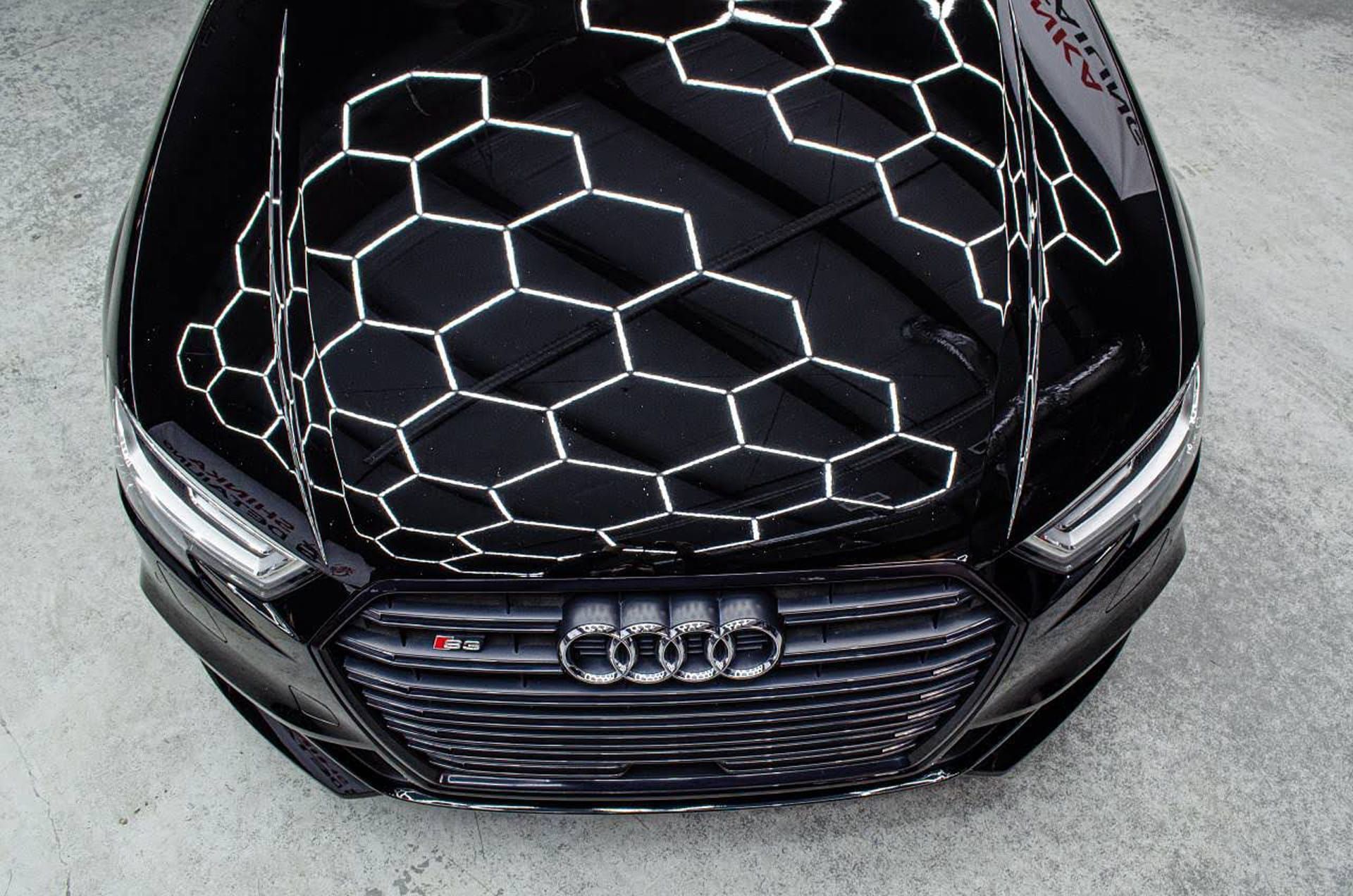 Black Audi car hood reflecting hexagonal shapes, with the car's front grille and headlights visible.
