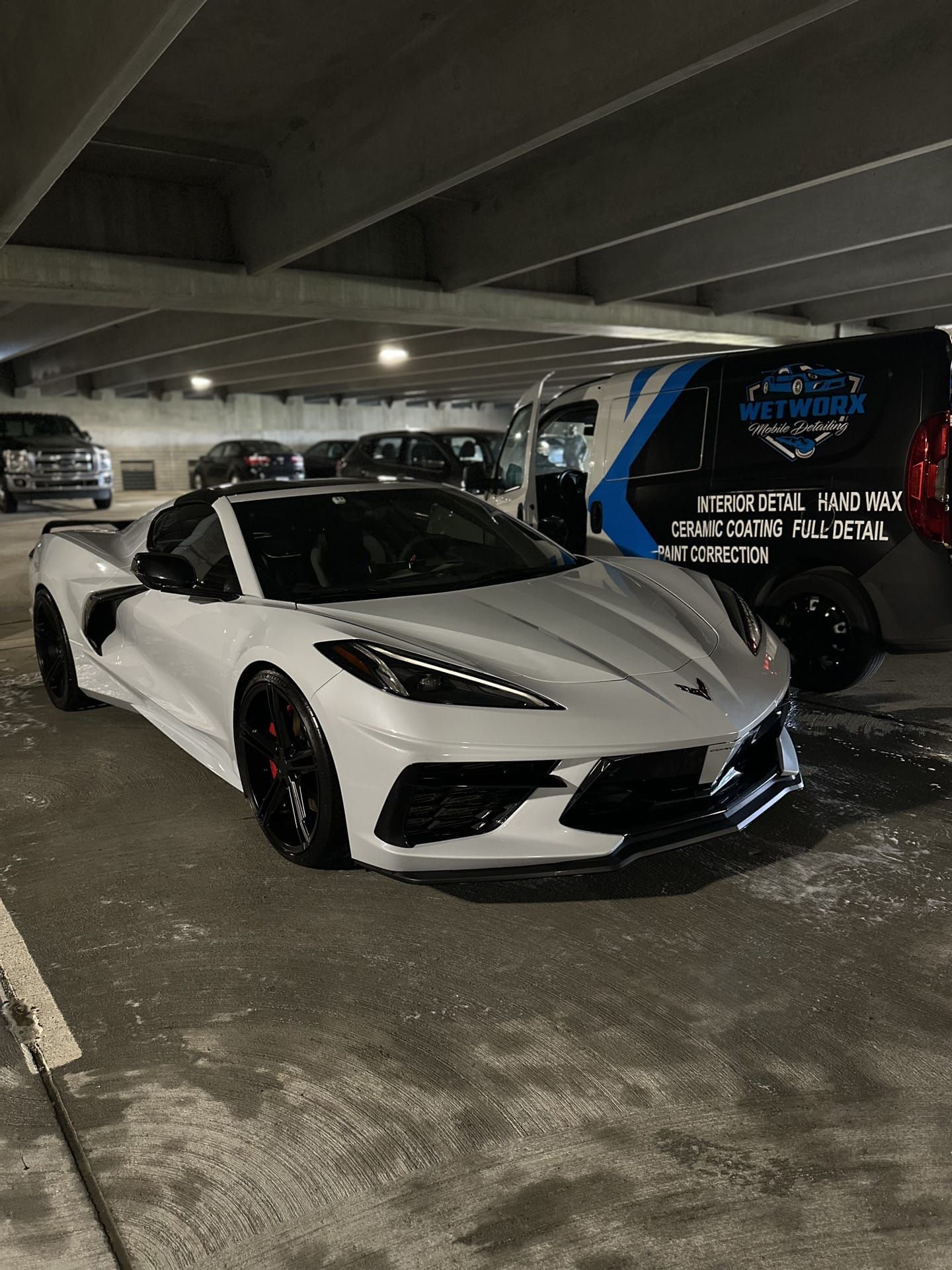 White sports car parked near a blue and white service van in a parking garage.