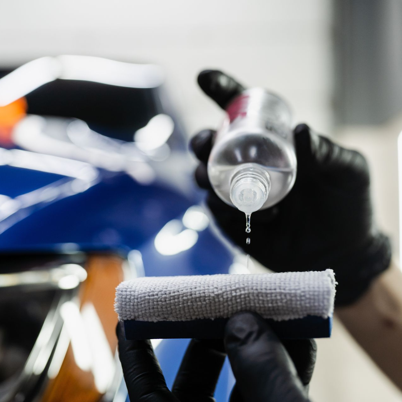 A person in black gloves applying liquid to a car's surface with a microfiber cloth.